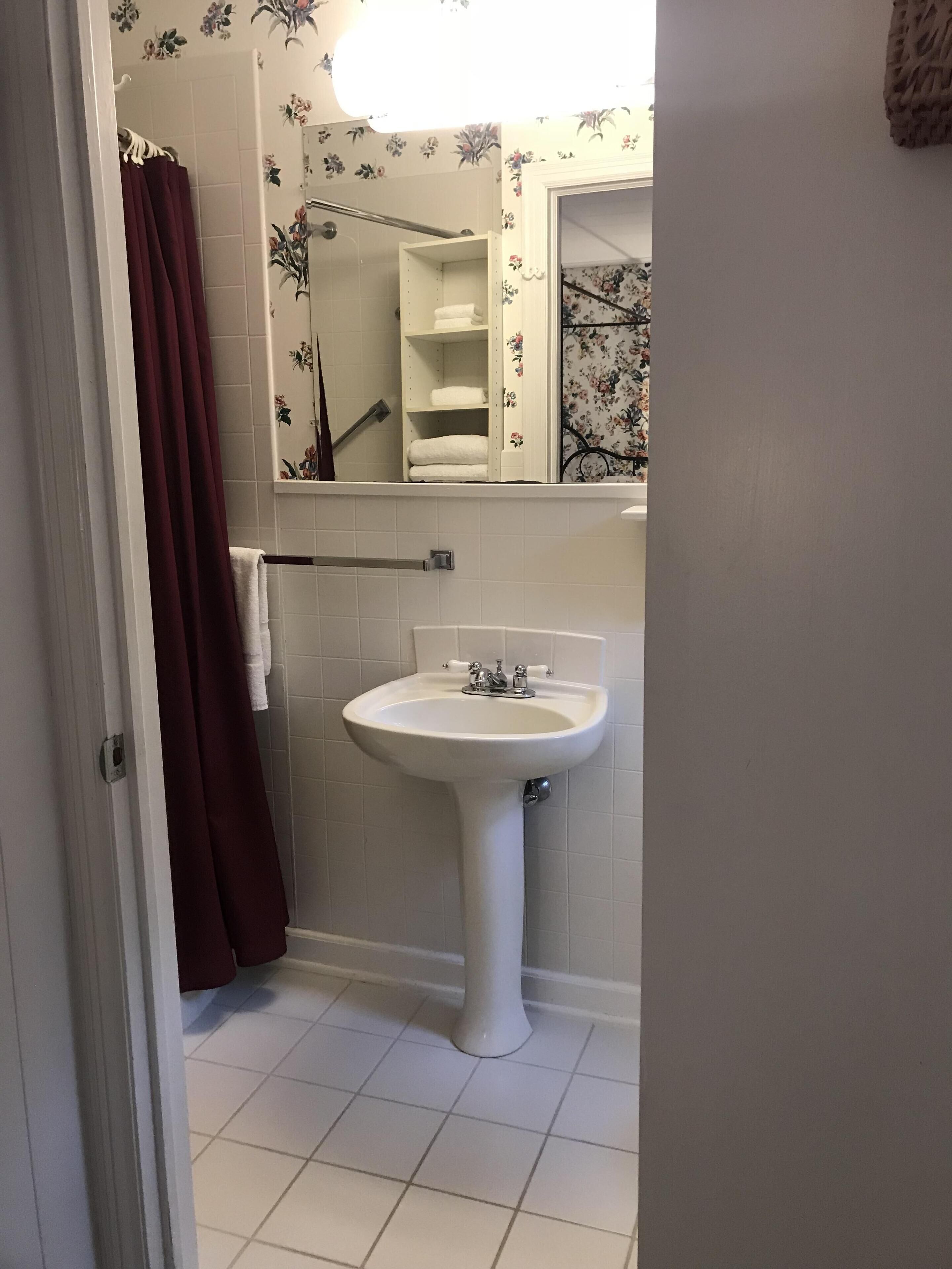 Un baño con lavamanos blanco, espejo y zona de ducha.