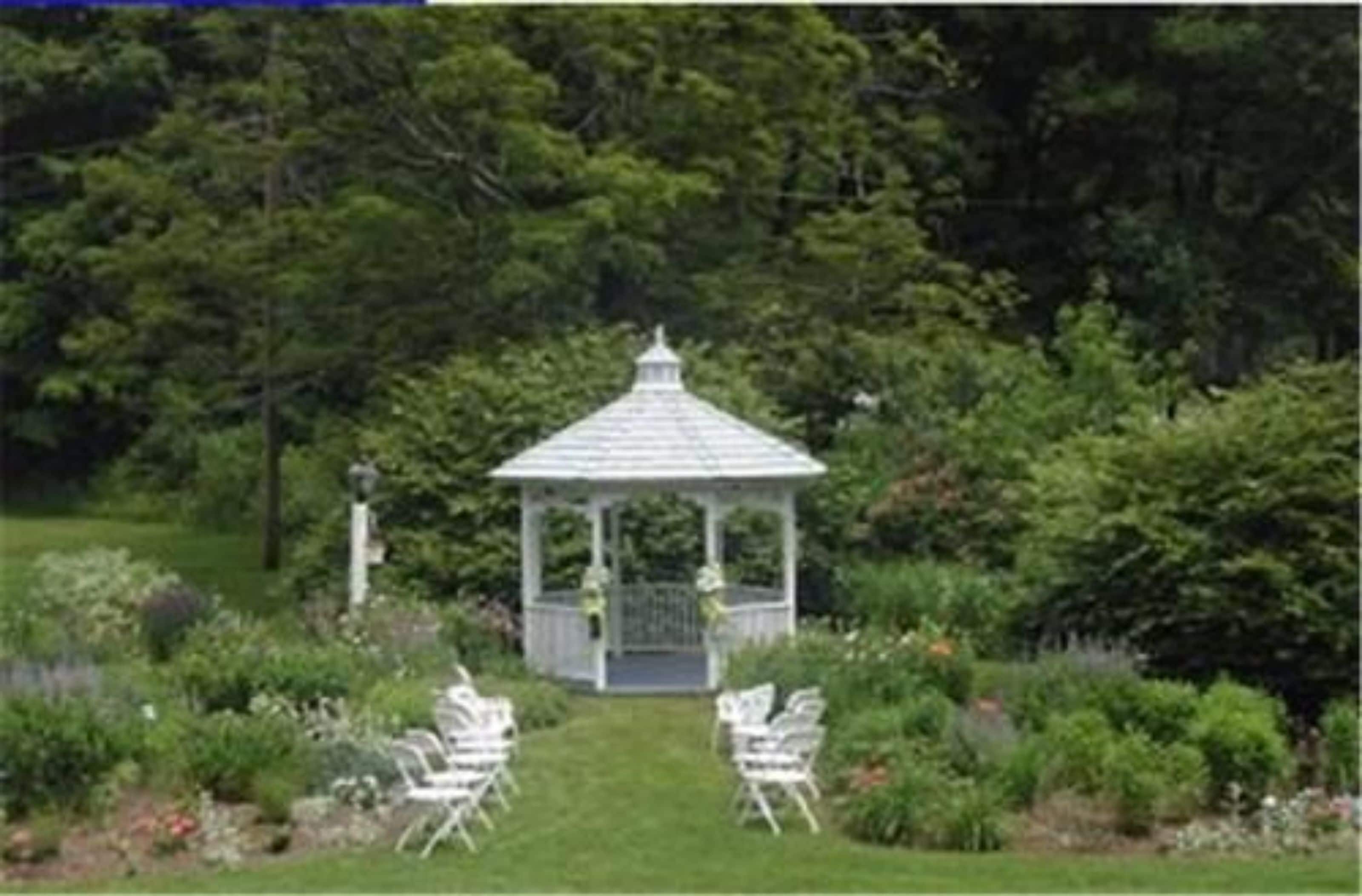 A gazebo with a white roof and a small porch, surrounded by lush greenery and a well-maintained garden.