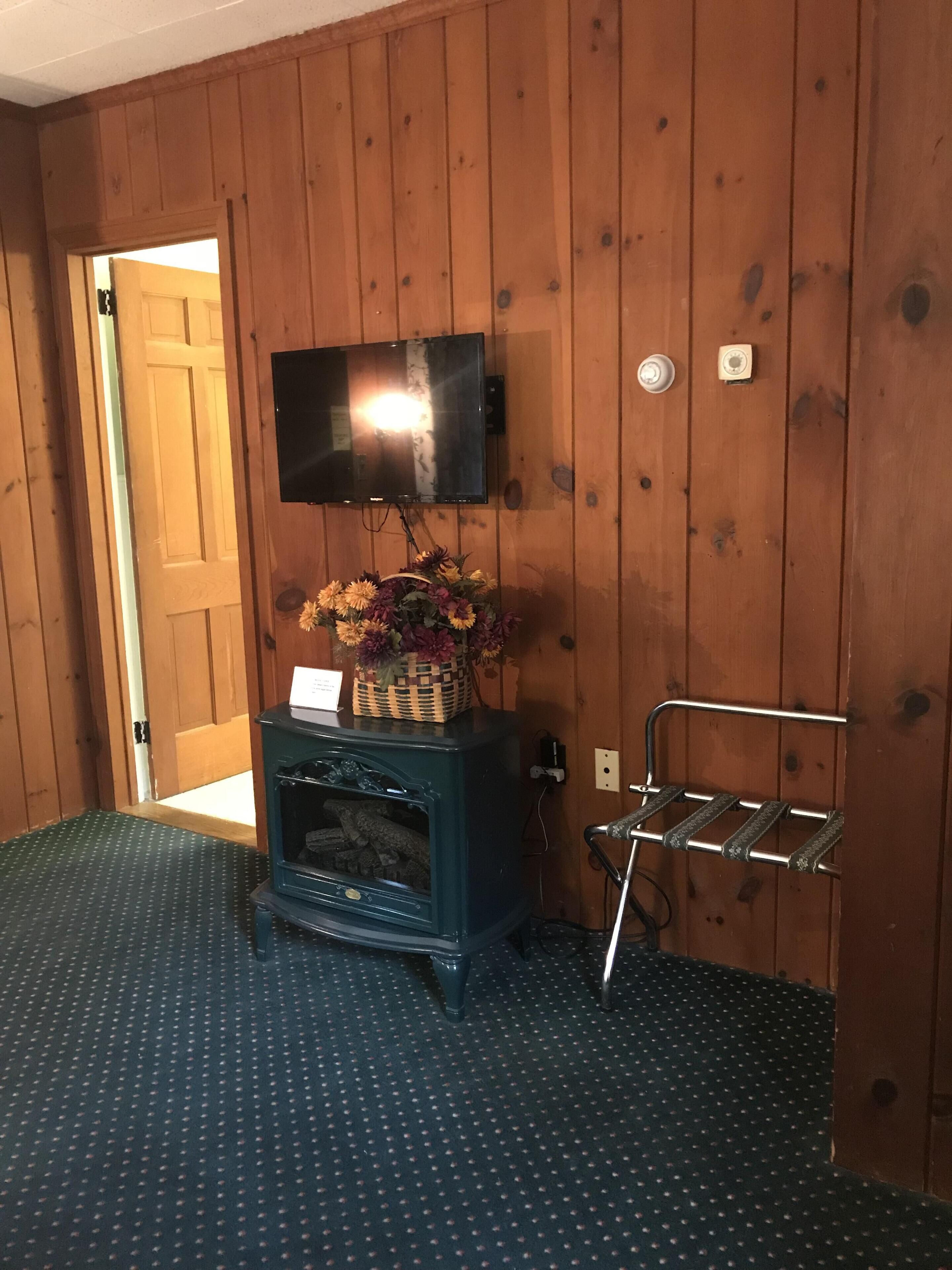Una habitación con paredes de madera, un televisor montado, un mueble bajo con una cesta de flores y una estantería de metal.