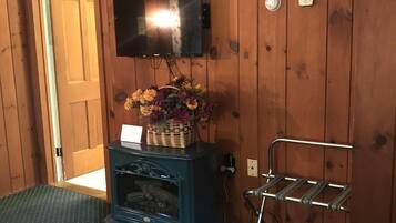 Una habitación con paredes de madera, un televisor montado, un mueble bajo con una cesta de flores y una estantería de metal.
