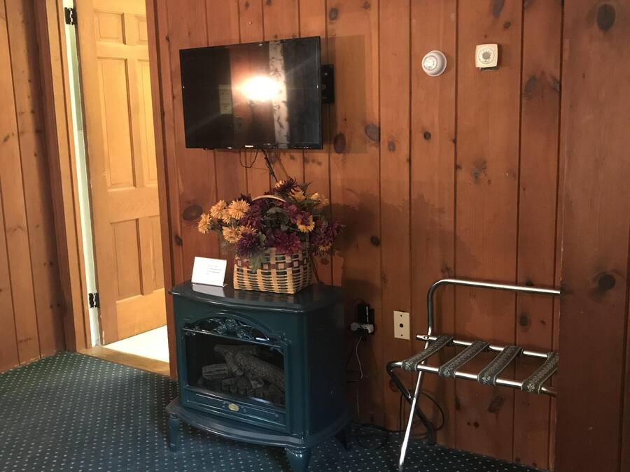 Una habitación con paredes de madera, un televisor montado, un mueble bajo con una cesta de flores y una estantería de metal.