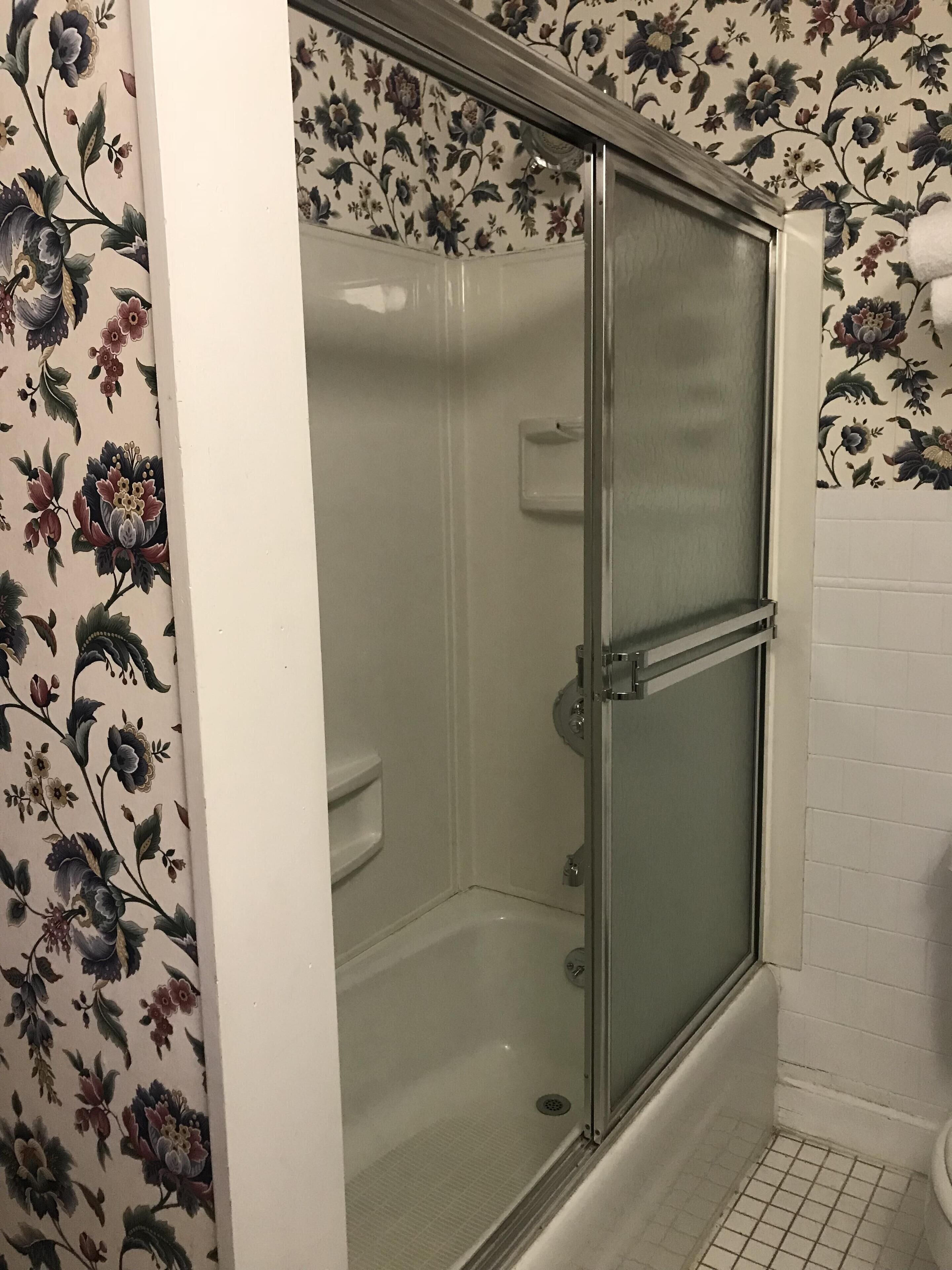 A shower enclosure with a glass door, a toilet, and a tiled floor.