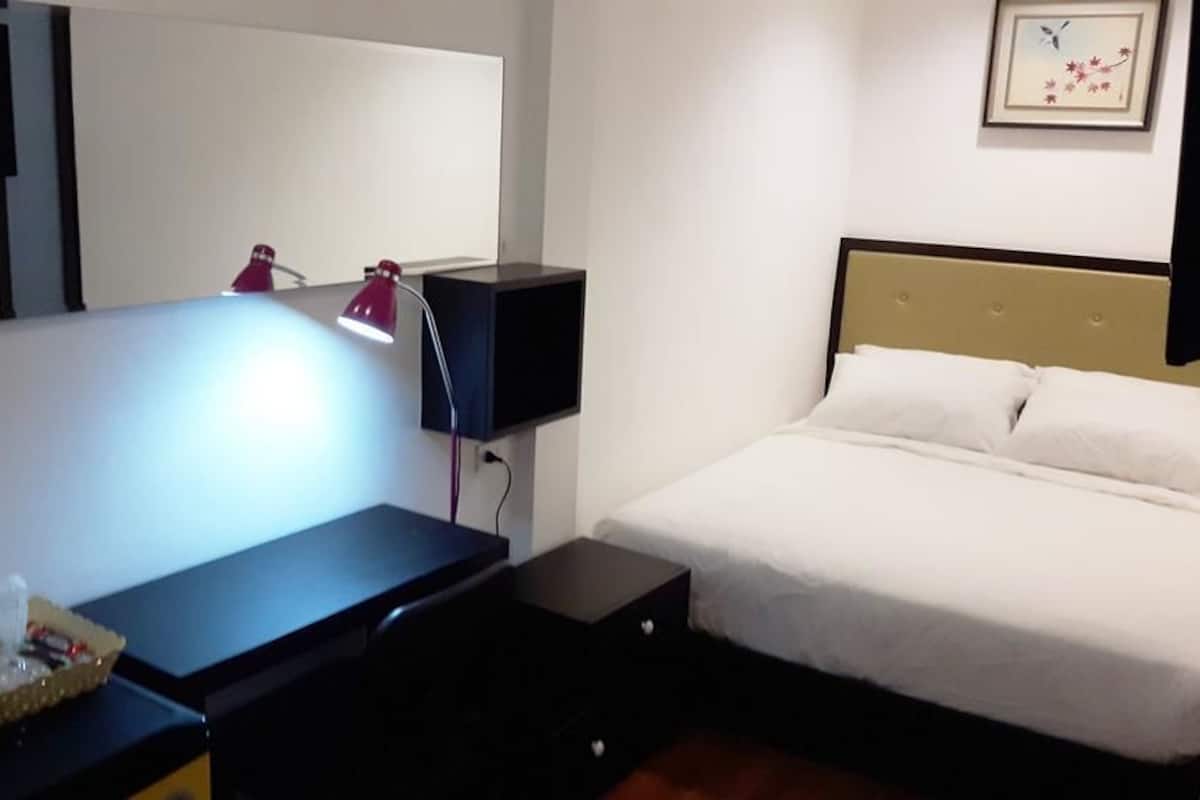 A hotel room with a bed, a desk with a lamp, a small table, and a wall-mounted TV.