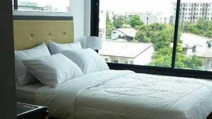 Una cama bien hecha en una habitación con un ventanal que ofrece vistas a edificios y zonas verdes.