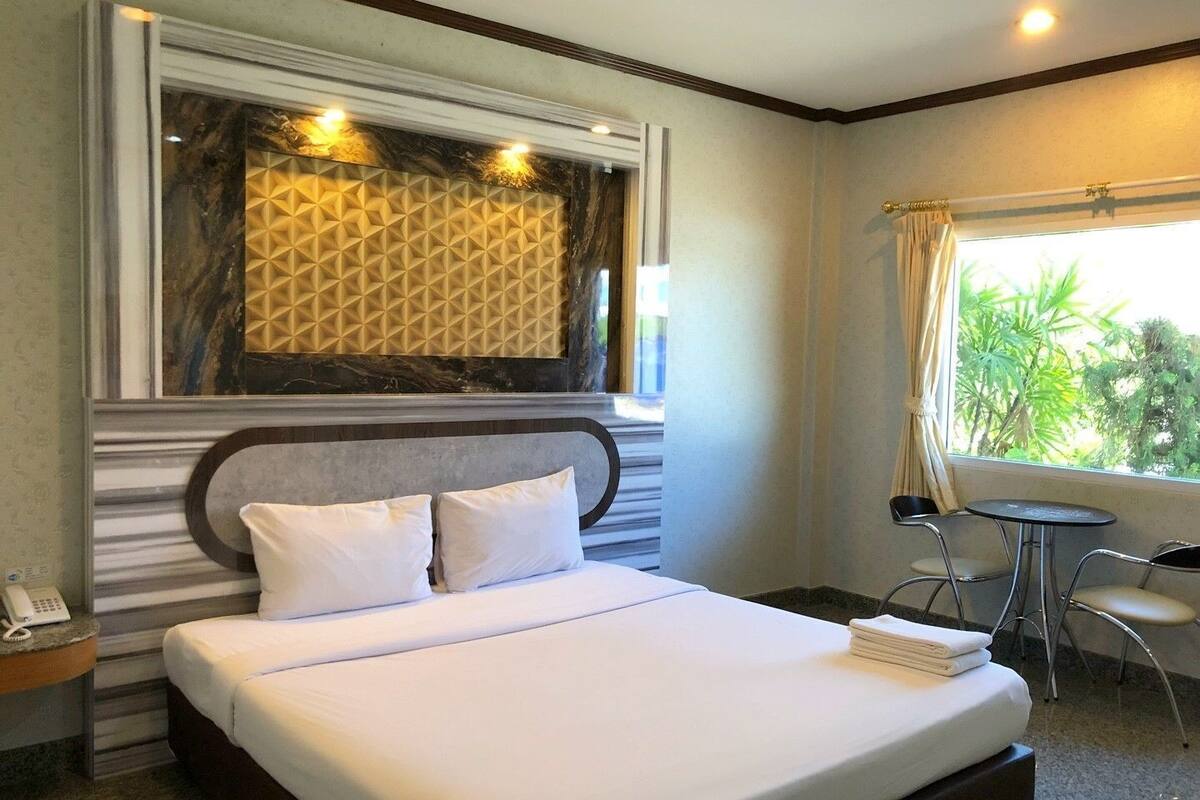 A hotel room with a bed, bedside table, and a window with a view of greenery.