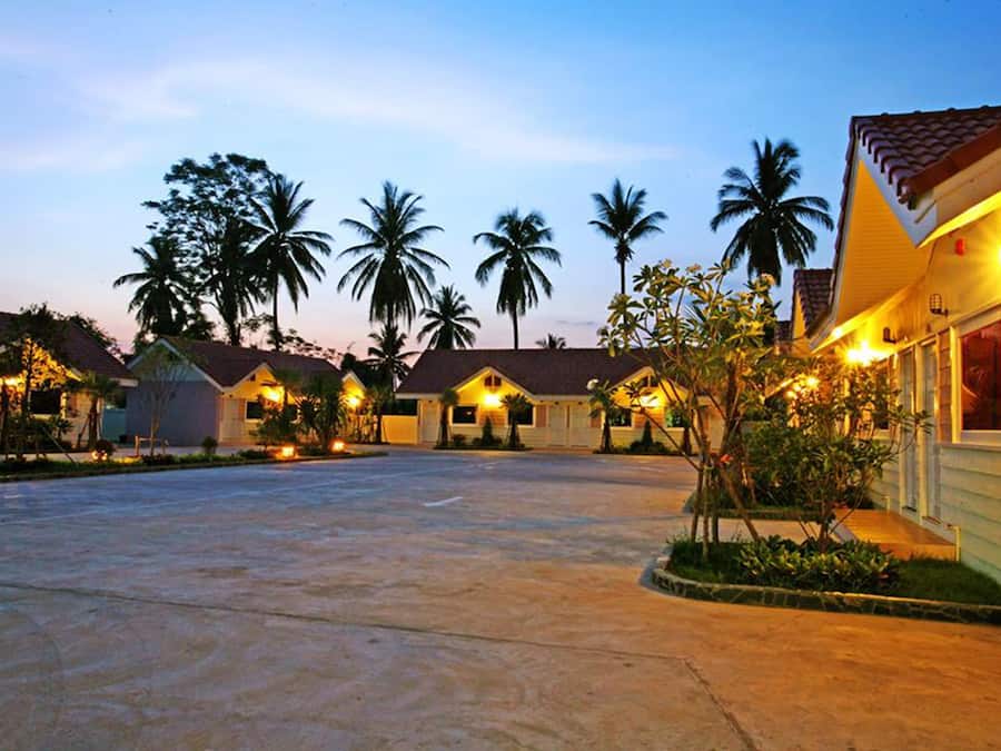 A row of single-story buildings with a paved driveway and palm trees in the background.