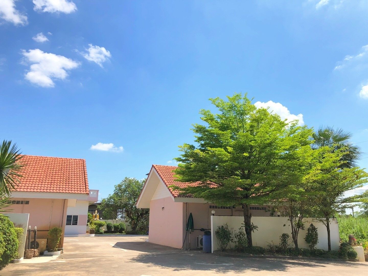 Un quartier résidentiel composé de deux maisons : l’une avec un toit recouvert de tuiles rouges et l’autre avec une façade rose, le tout entouré de verdure et surplombé par un ciel bleu clair.