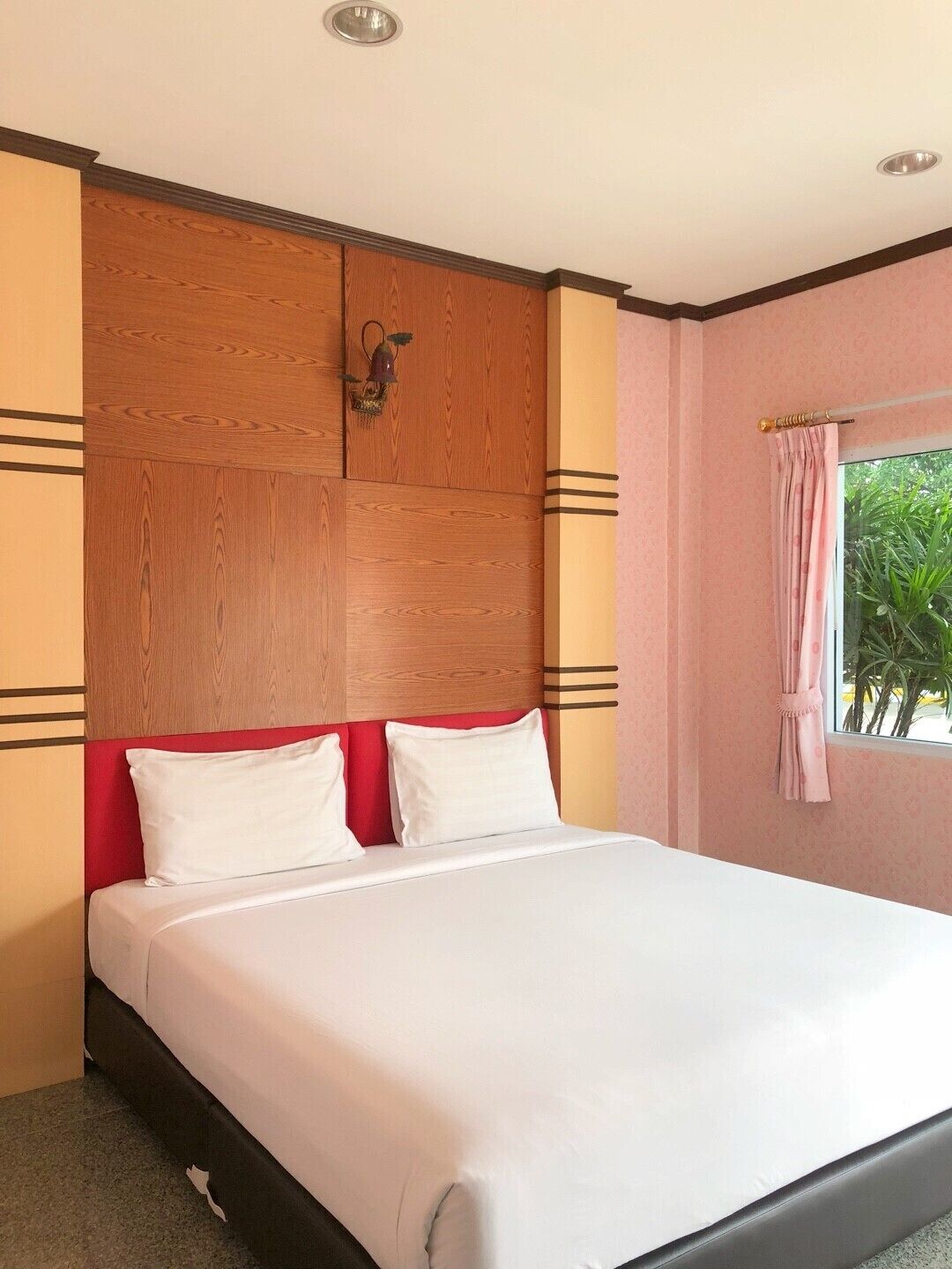 A hotel room with a large bed, wooden headboard, and a window with curtains.