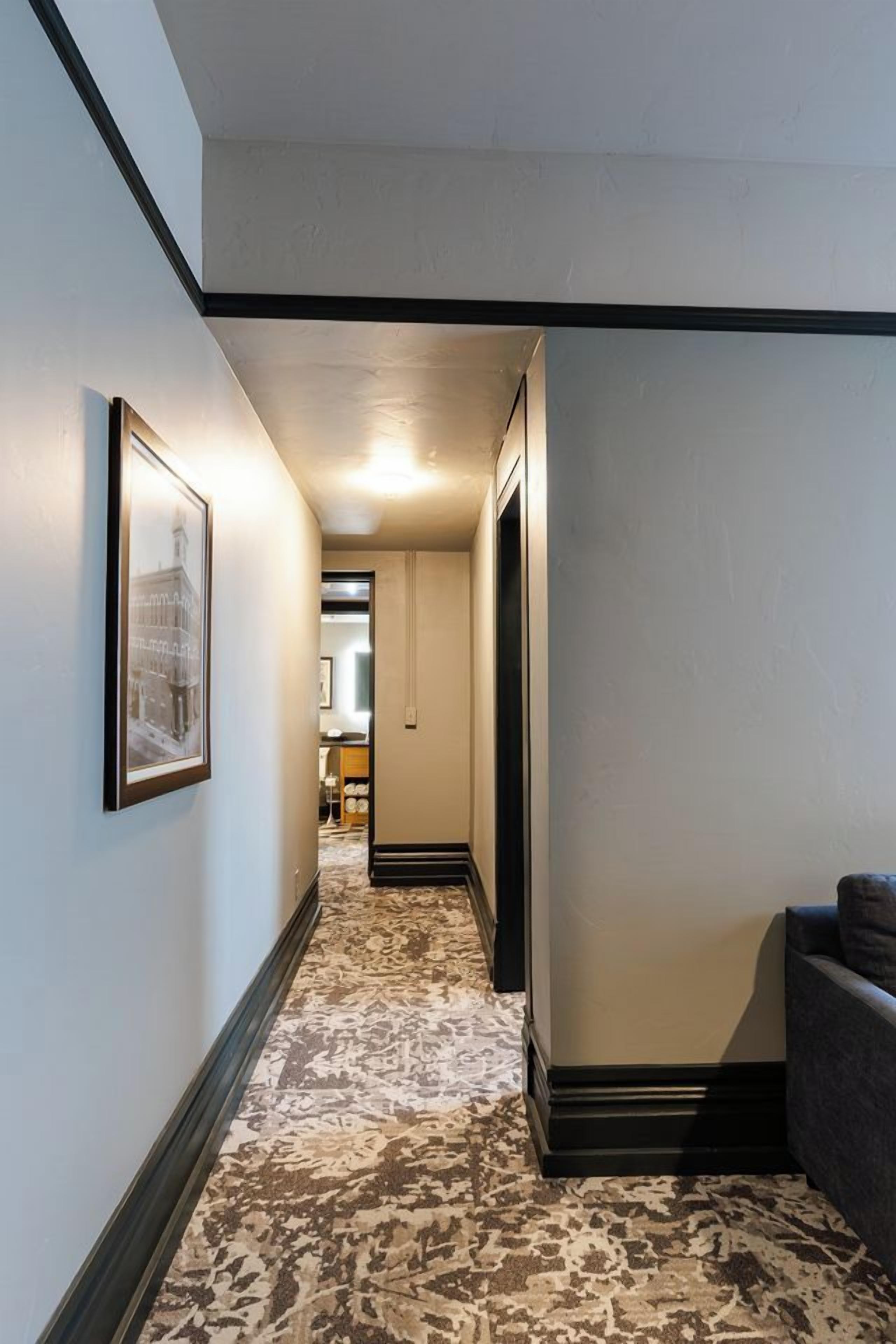 A hallway with patterned carpet, framed artwork on the wall, and a sofa in the corner.