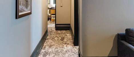A hallway with patterned carpet, framed artwork on the wall, and a sofa in the corner.