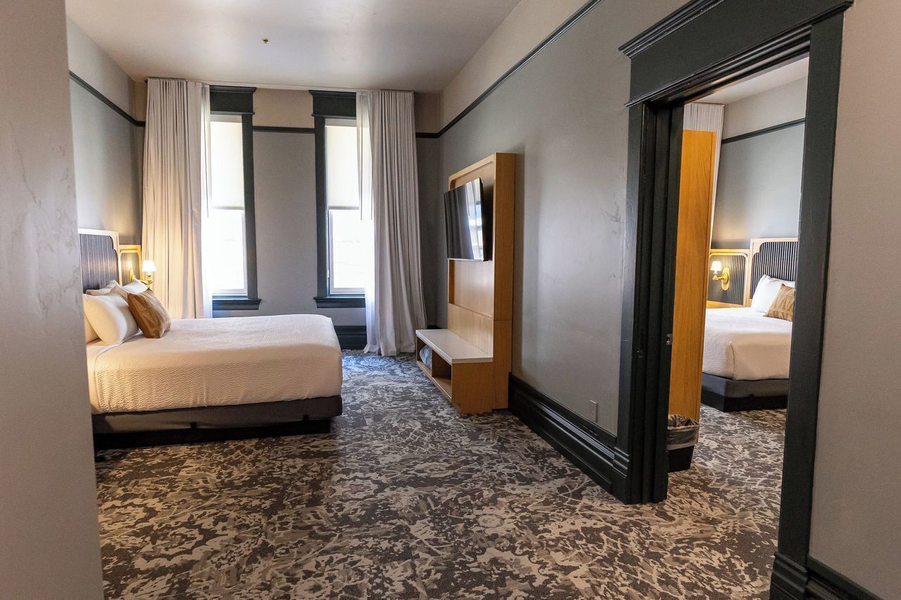 A hotel room with a bed, a TV, a small seating area, and a large mirror.