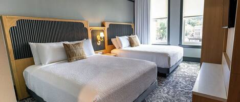 A hotel room with two beds, a large window, and a wooden wardrobe.