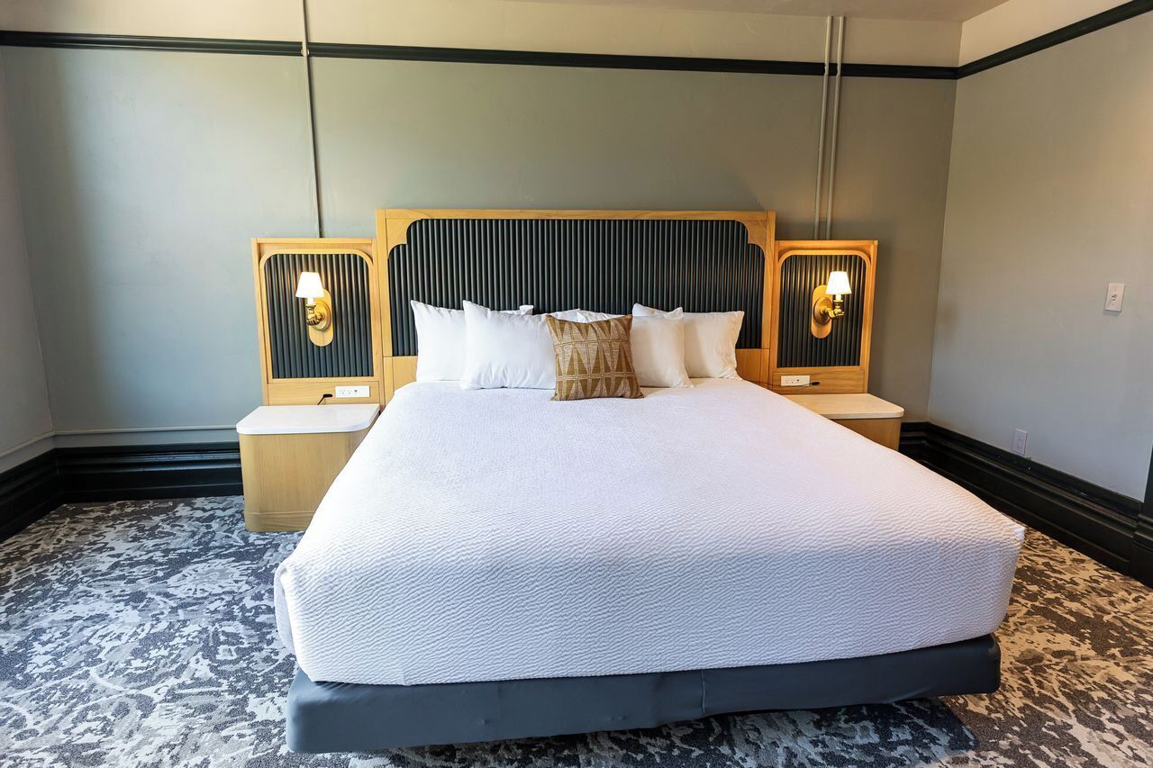 A hotel room with a large bed, two bedside tables, and wall-mounted lamps.