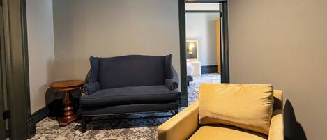Une pièce avec un canapé foncé, un fauteuil jaune et un tapis à motifs.