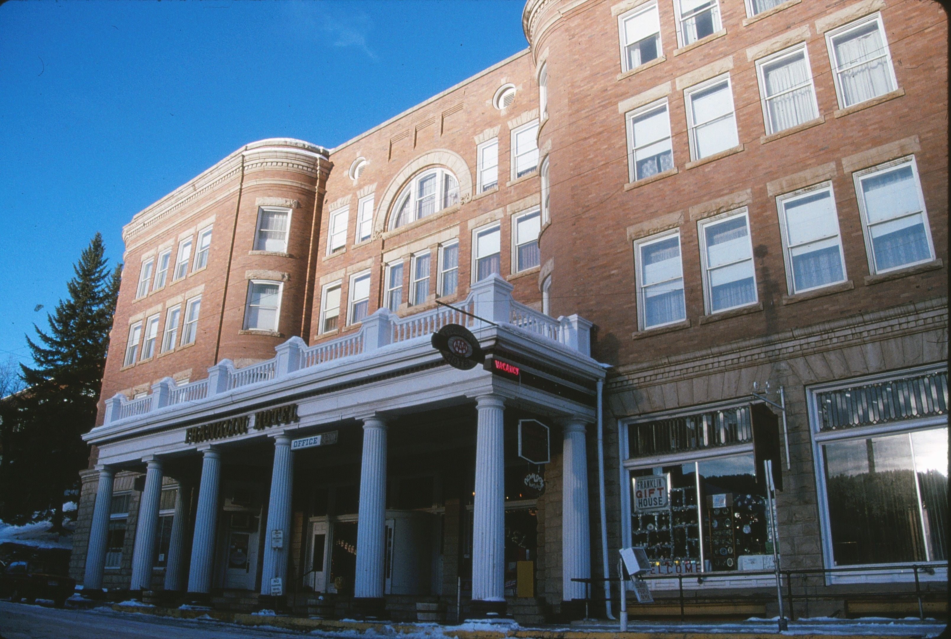 A historic building with a prominent corner entrance, large windows, and a balcony with columns.