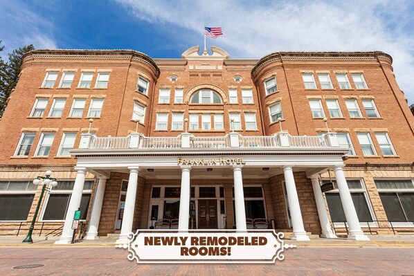 A historic brick building with a classic facade, a prominent American flag, and a sign indicating newly remodeled rooms.