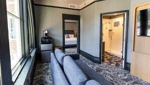 Quarto de hotel com sofá, pequena escrivaninha, cama e banheiro visível por uma porta aberta.