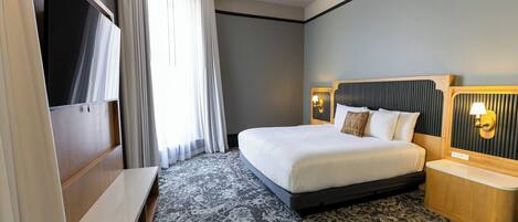 Una habitación de hotel con cama, mesitas de noche, un escritorio y una ventana con cortinas.