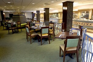 Un comedor de hotel con varias mesas y sillas, un mostrador de buffet y una planta decorativa.