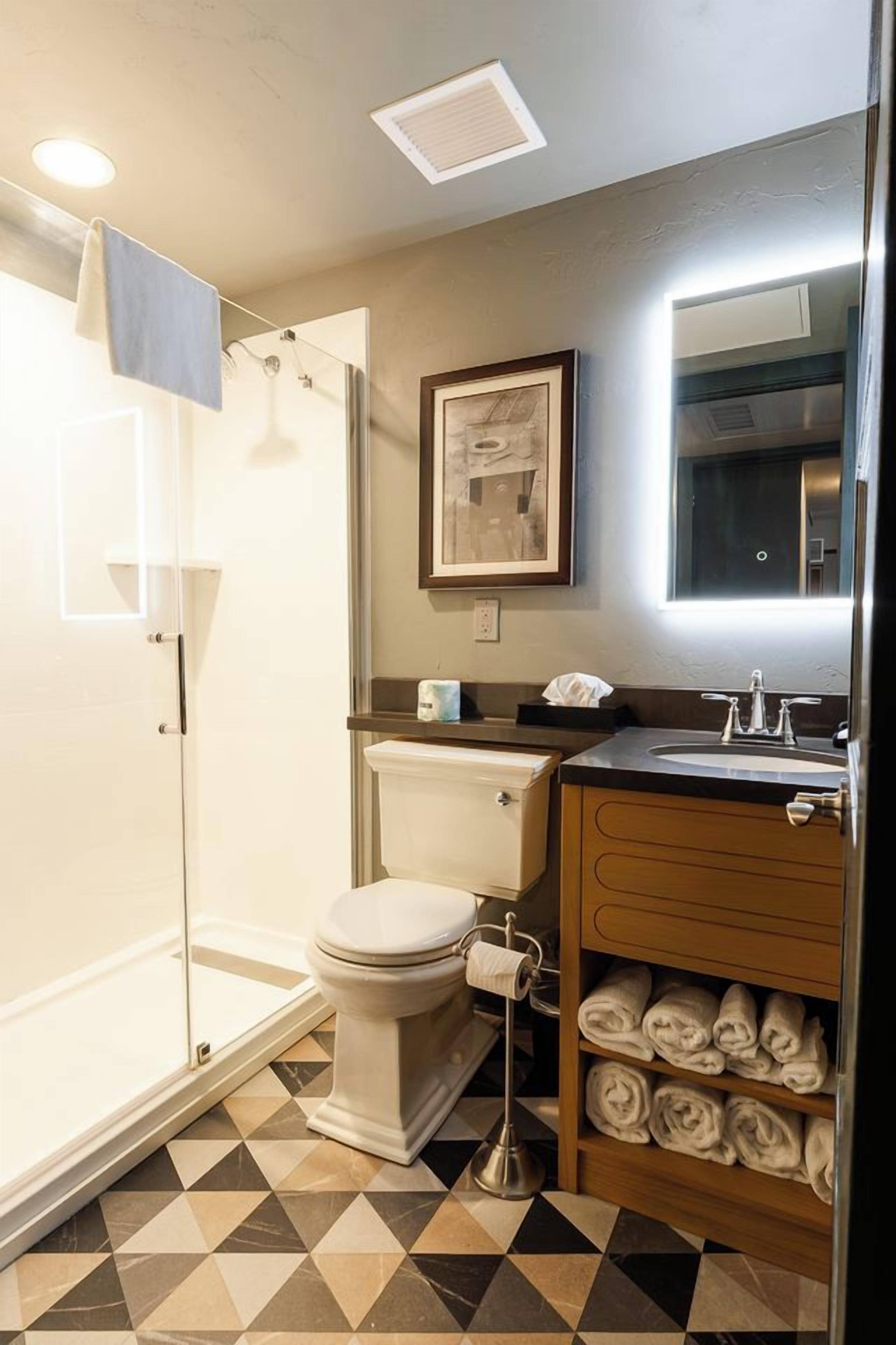 A bathroom with a shower, toilet, sink, and a towel rack with towels.
