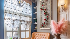 A room with a large window, a chandelier, a table with a lace tablecloth, a tufted leather chair, and a decorative vase with pink flowers. - So Funny (Hualien City)