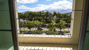 Un balcon donnant sur un espace paysager, des arbres et des montagnes lointaines.