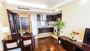 A modern kitchen with dark cabinets, a microwave, and a sink. There is a dining area with a table and chairs, and a living area with a sofa and a TV.