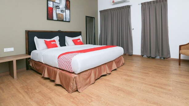 A hotel room with a large bed, a headboard, a bedside table, a wall-mounted air conditioner, and a window with curtains. - OYO 89915 East Mount Hotel (Kukup)