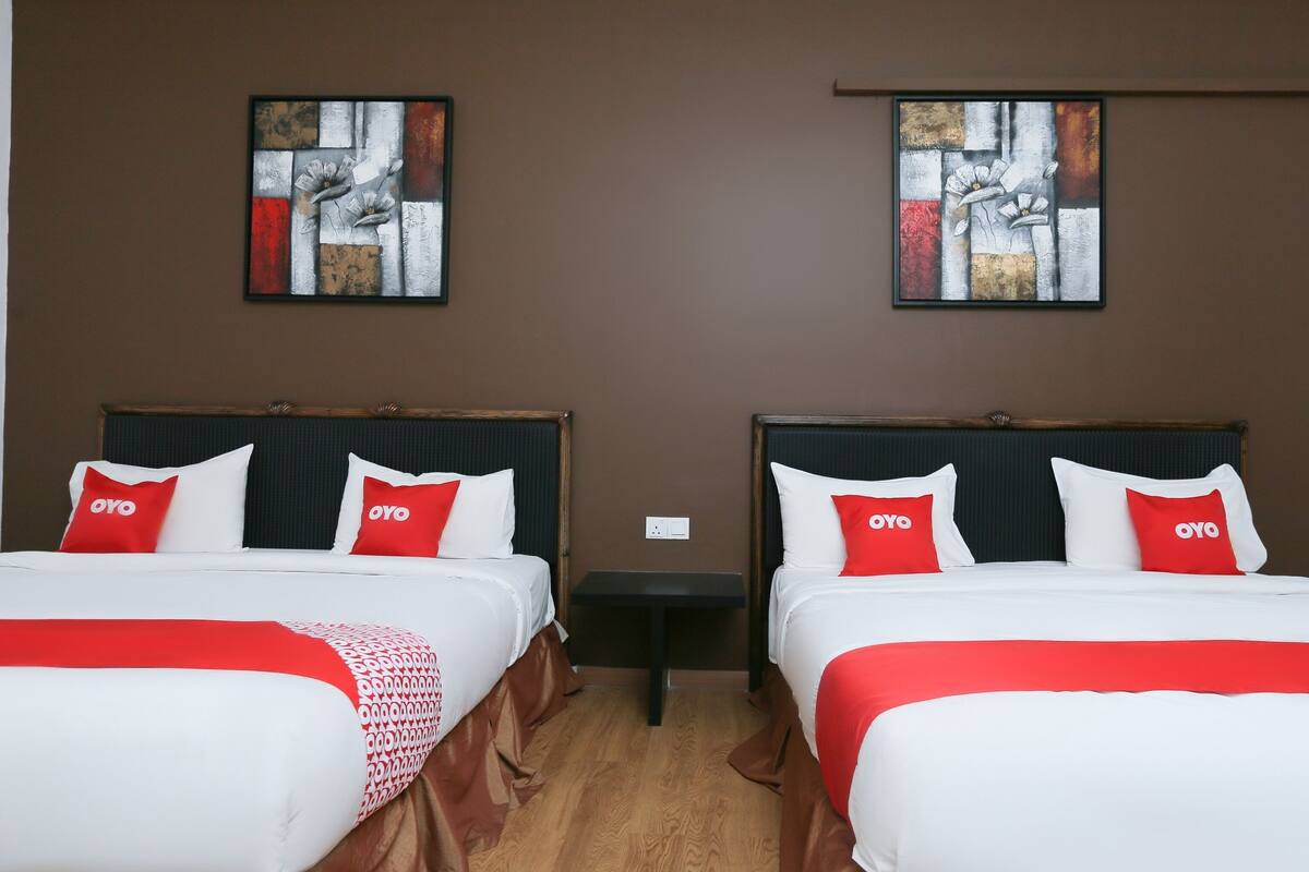 A hotel room with two beds, each with white bedding and red pillows, and abstract artwork on the walls.