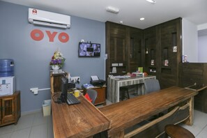 A reception area with a wooden desk, a water dispenser, a flower vase, and a mounted television. - OYO 89915 East Mount Hotel (Kukup)