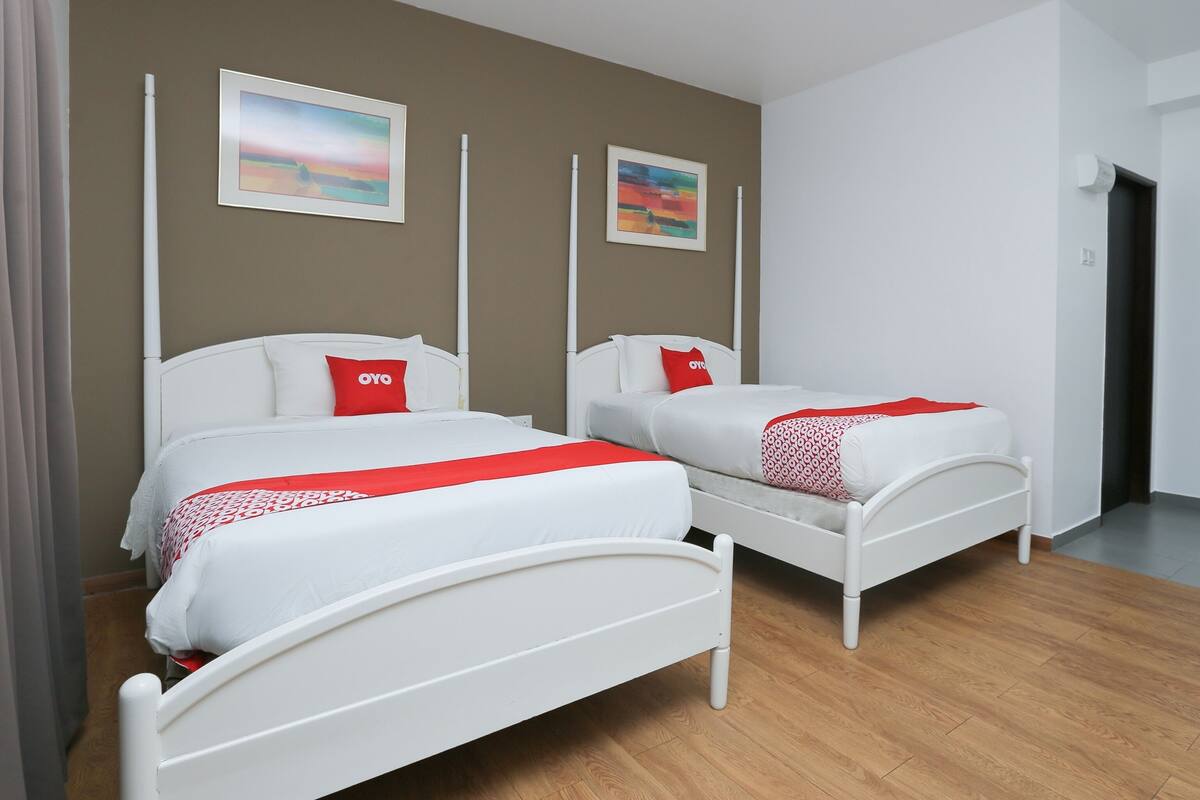 A hotel room with two single beds, each with a white frame and red accents, positioned against a brown wall with two framed pictures.