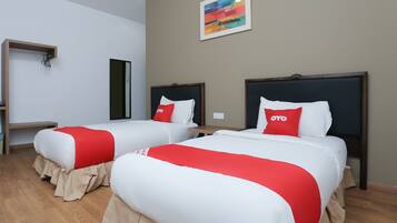 A hotel room with two beds, each with white bedding and red accents, a wooden floor, a painting on the wall, and a small table with a lamp.