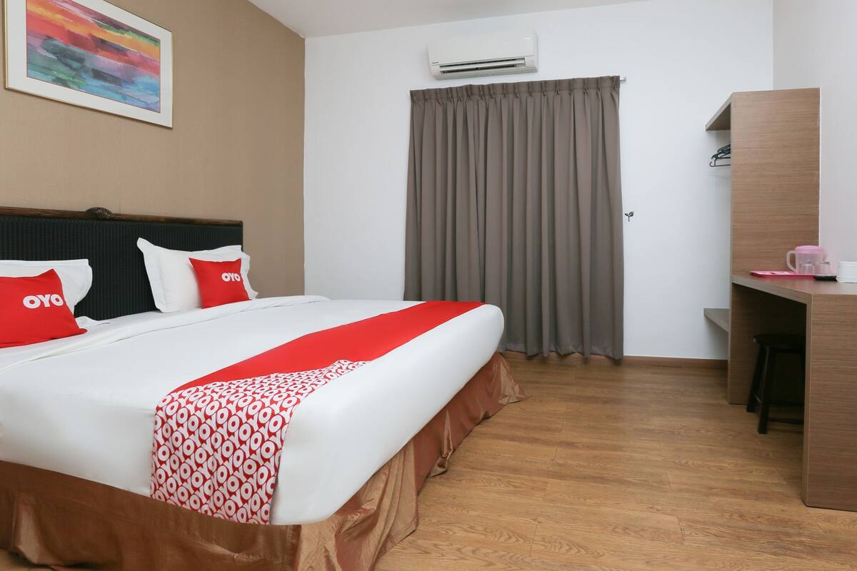 A hotel room with a bed, a desk, a chair, an air conditioner, and a curtain.