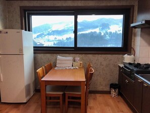 Eine Küche mit einem Holztisch, Stühlen, einem Kühlschrank, einem Herd und einem Fenster mit Blick auf eine verschneite Landschaft.