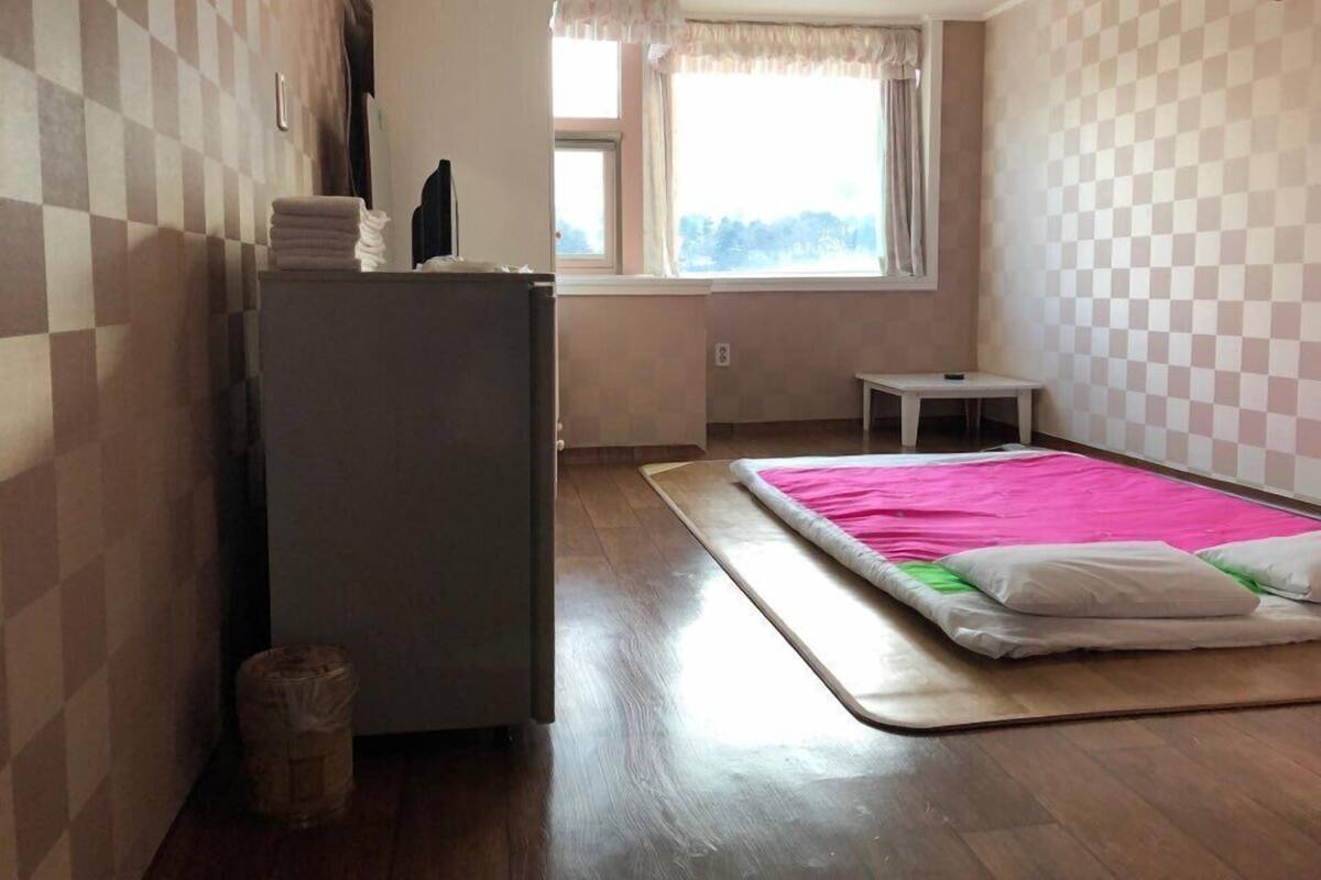 A small room with a bed, a desk, a refrigerator, and a window.