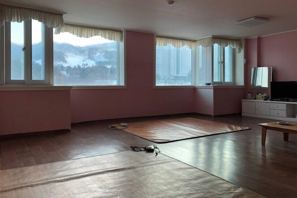 A room with large windows, a wooden floor, a television, and a white cabinet.