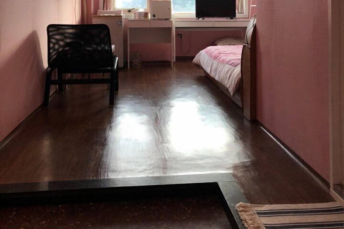 A small, pink-walled room with a bed, a desk with a computer, and a chair.