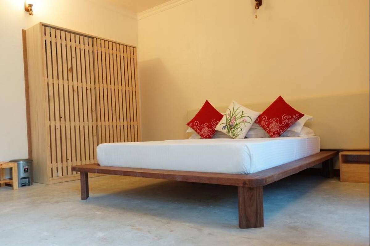 Un lit simple avec un cadre en bois et un matelas blanc, deux oreillers rouges et une table de chevet en bois.