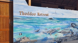 A mural of a tropical ocean scene with the text "Thoddoo Retreat" on a wooden door. - Thoddoo Retreat (Thoddoo)
