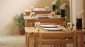 Una fila di tavoli di legno con piatti, bicchieri e posate, che suggerisce una sala da pranzo.
