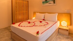 Un letto rifatto con cura, con copripiumino bianco, decorazioni floreali rosse e una piccola lampada da comodino.