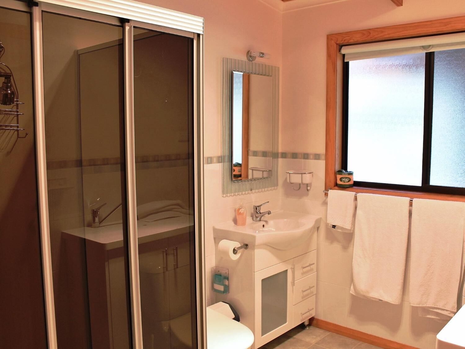 Een badkamer met een douchecabine van glas, een wastafel met spiegel en een raam met houten kader.