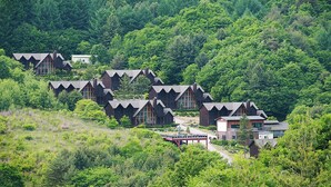 A cluster of log cabin-style buildings surrounded by dense forest. - Chalet Resort (Pyeongchang)