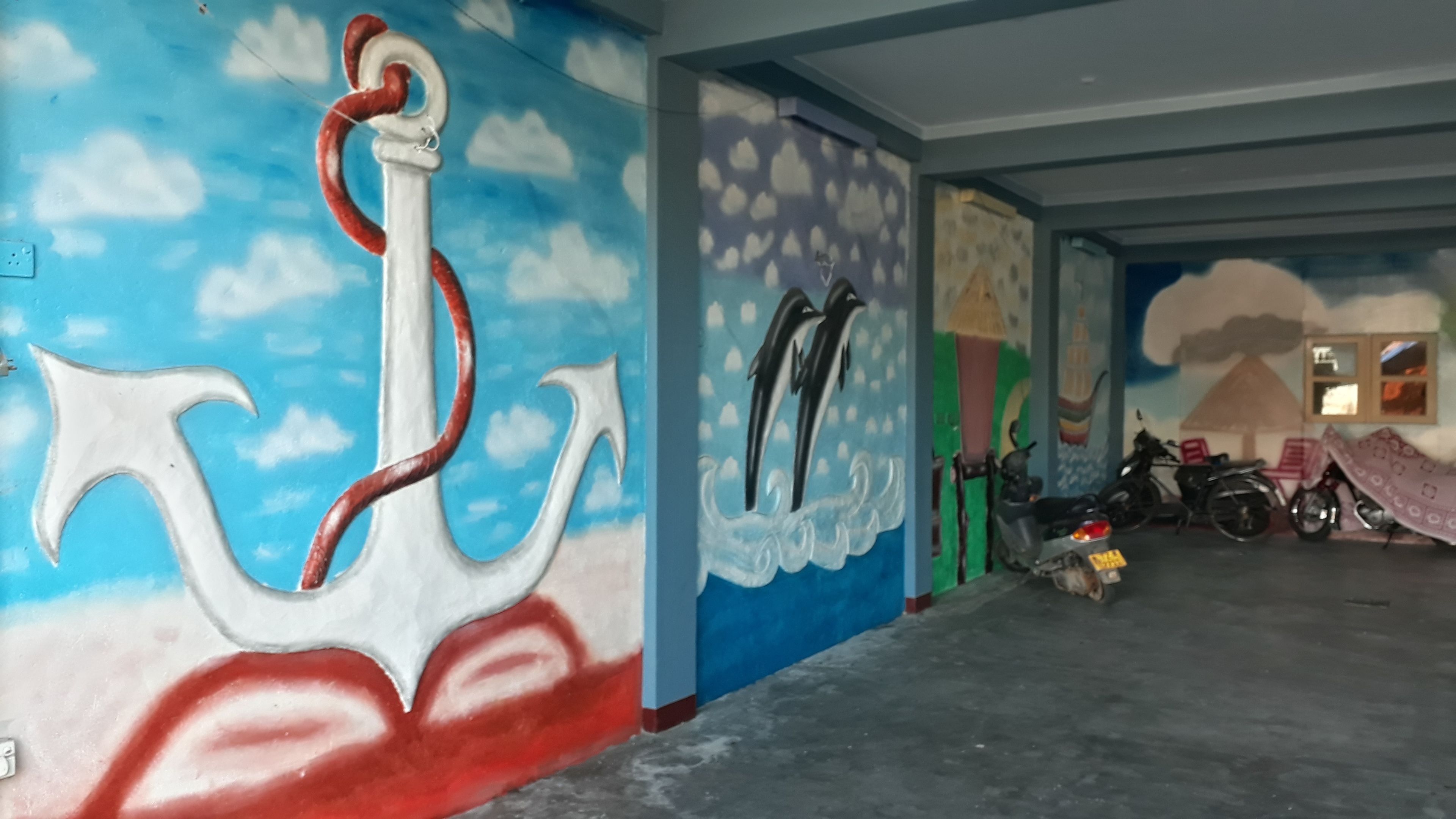 A room with a mural of an anchor and dolphins, a motorcycle, and a scooter parked in the corner.