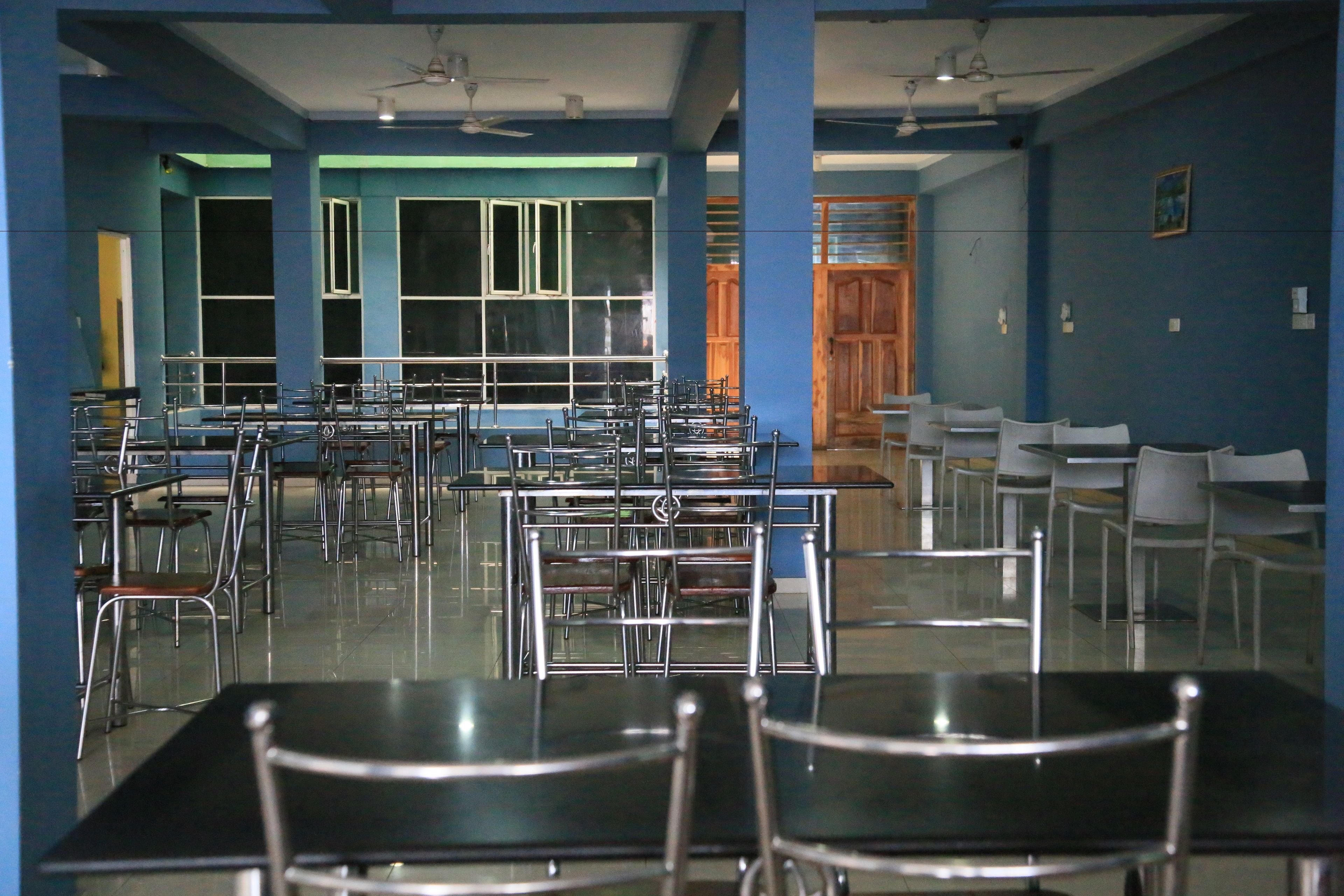 A spacious dining area with multiple tables and chairs, large windows, and ceiling fans.