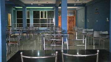 Un vaste espace dédié à la salle à manger, avec de nombreuses tables et chaises, de grandes fenêtres et des ventilateurs de plafond.