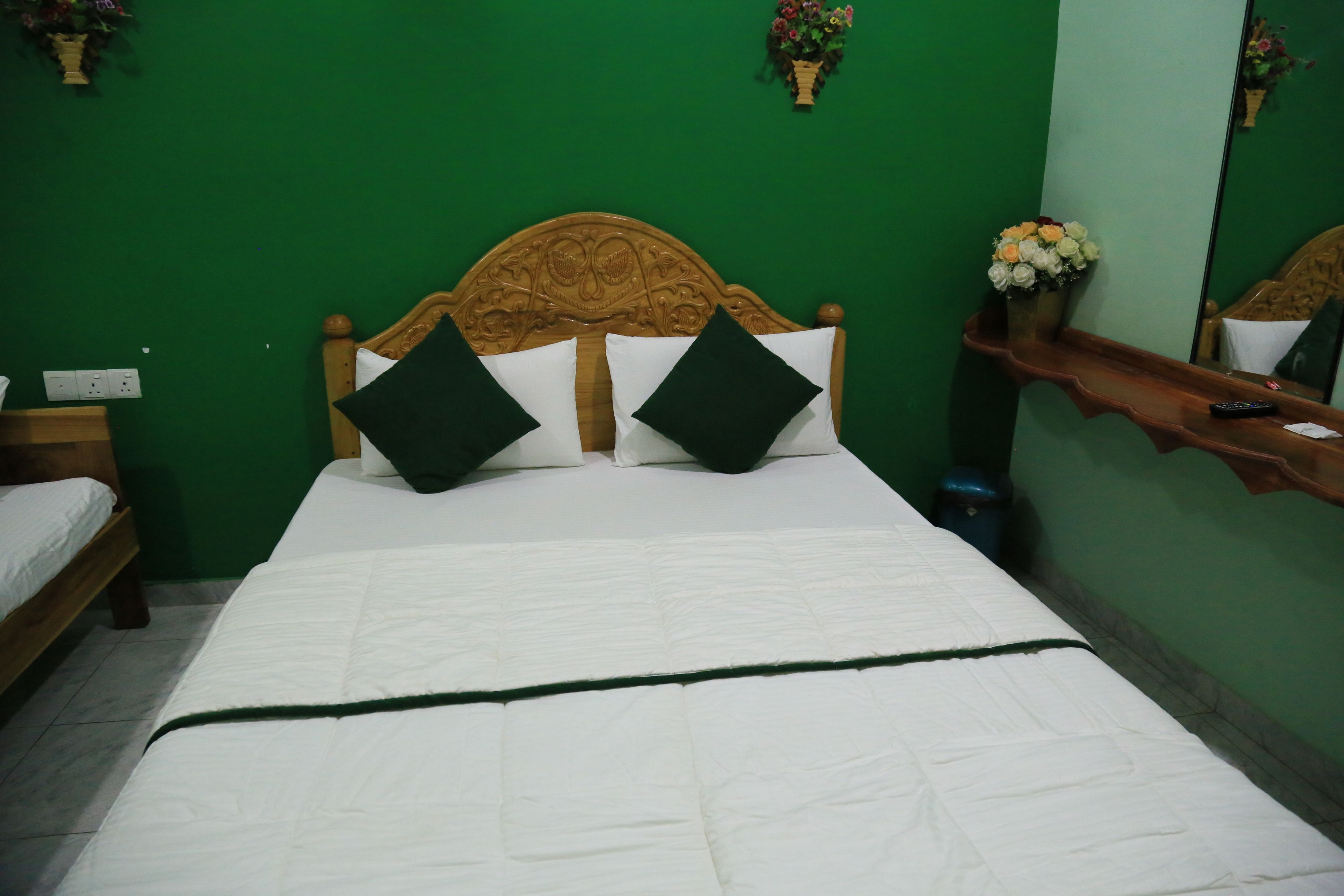 Een keurig opgemaakt bed met een houten hoofdbord, twee zwarte kussens en een groene dekbedovertrek.