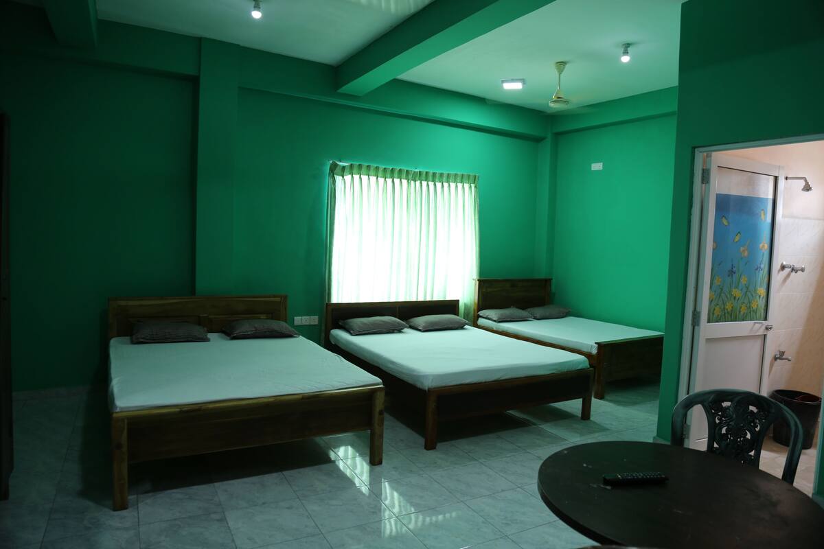 A room with three wooden beds, a small round table, and a window with curtains.