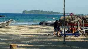 Una playa con barcos, una estructura de paja y una isla distante.