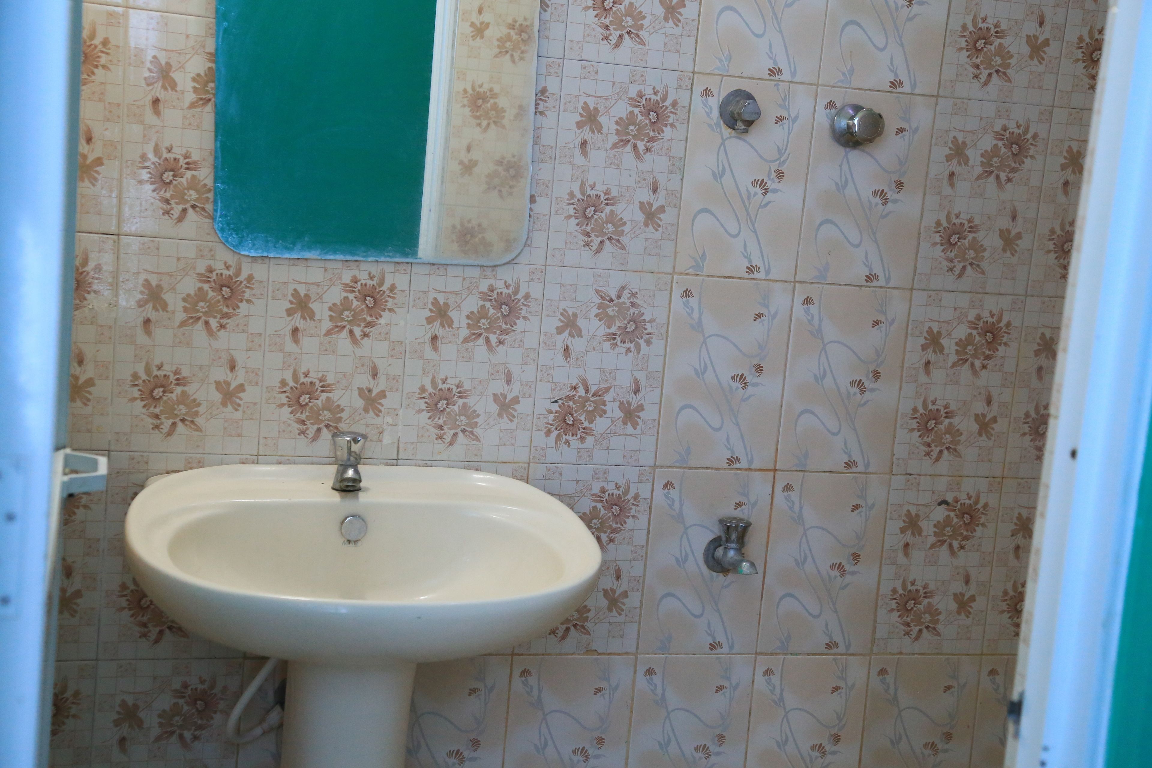 A bathroom with a white sink, floral patterned tiles, and a green shower curtain.